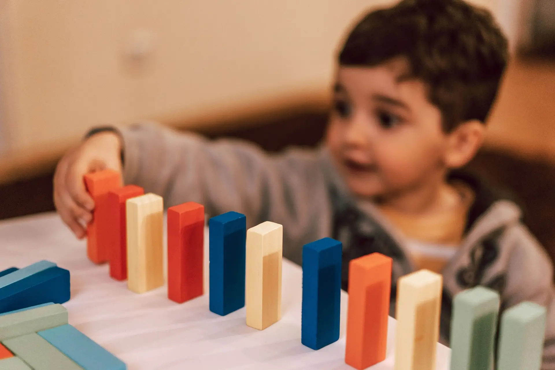 Un niño coloca en fila bloques de madera de colores sobre una mesa.