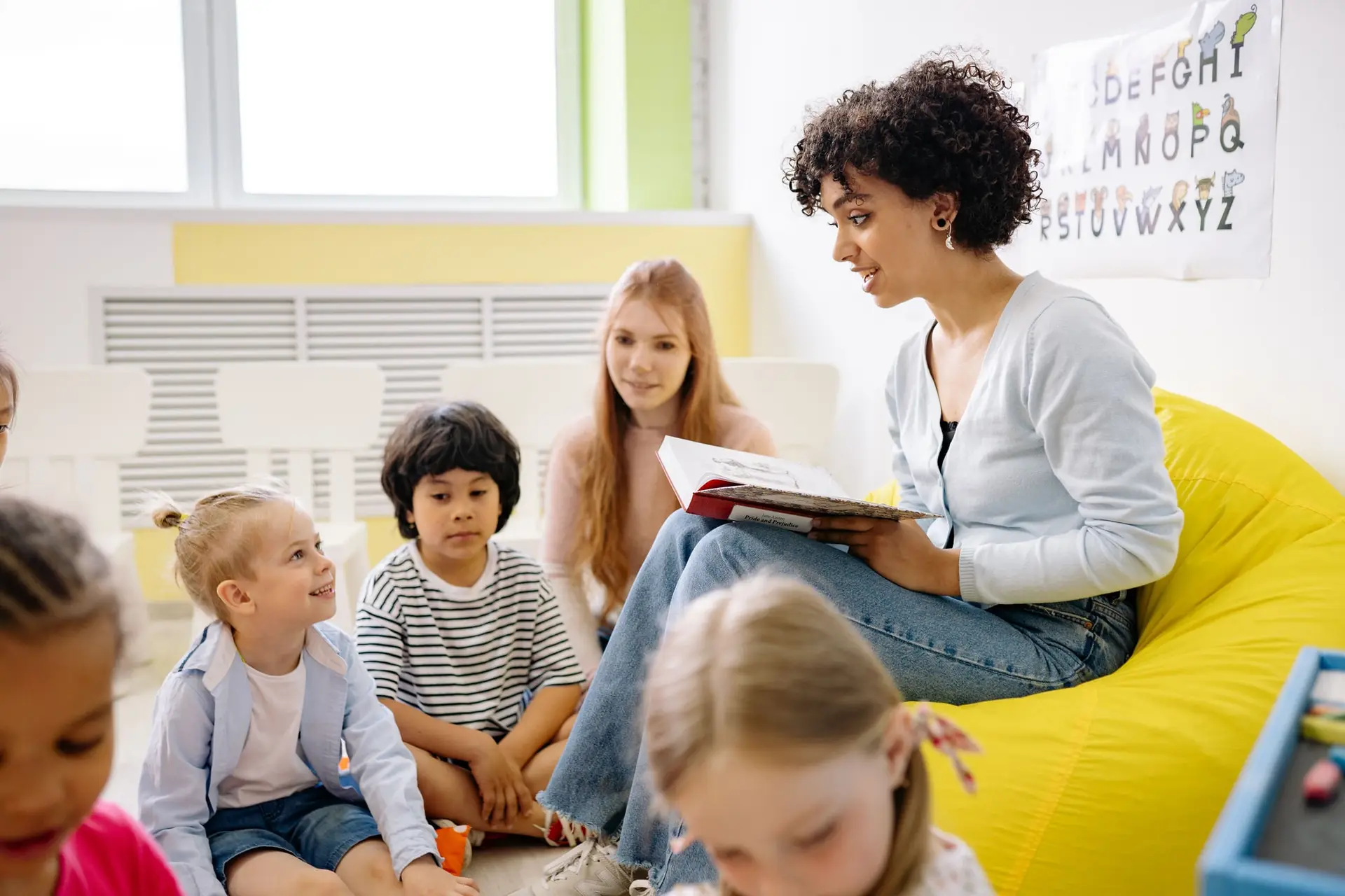 Una docente lee un libro a un grupo de niños sentados en semicírculo.