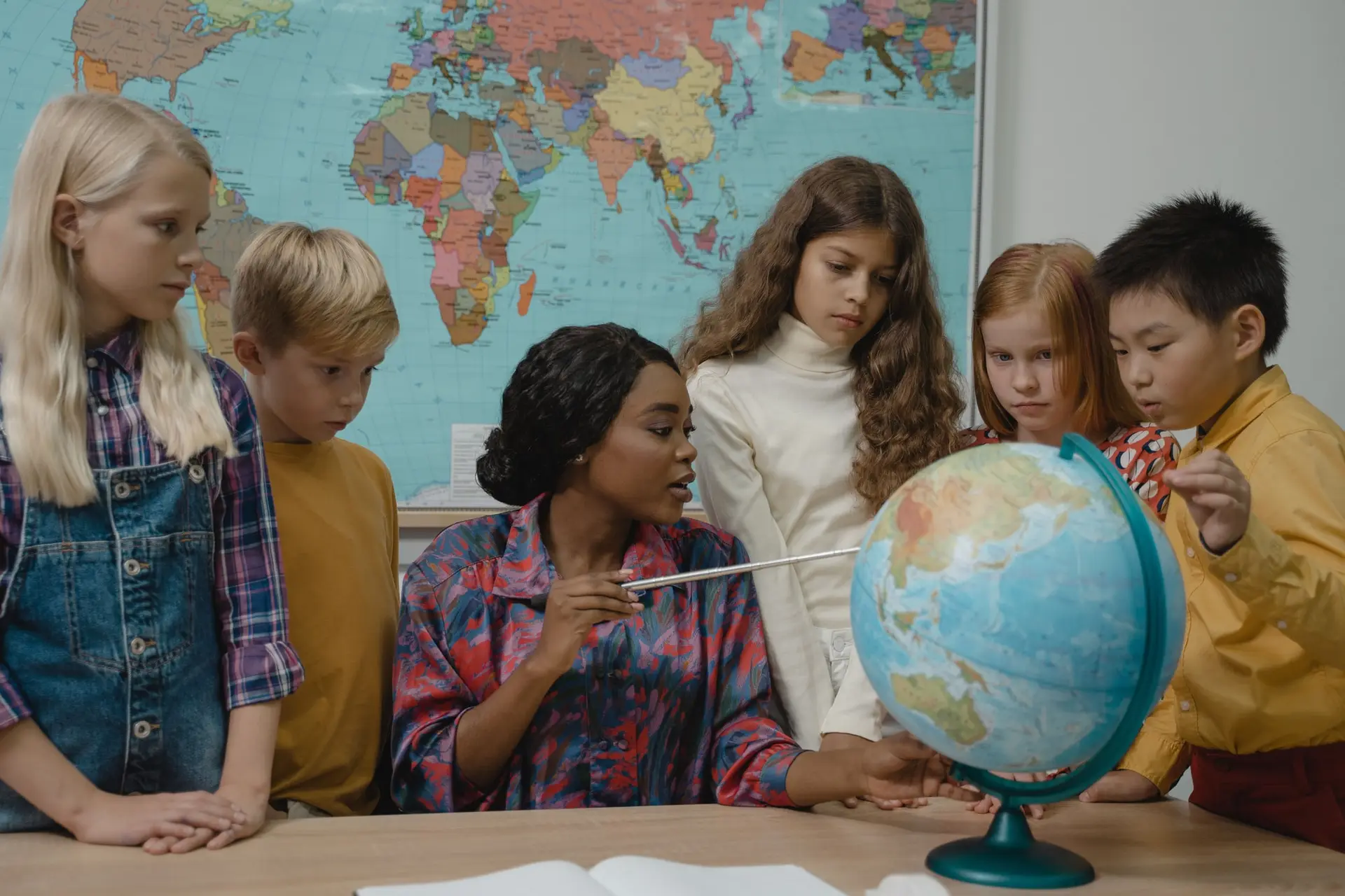 Un grupo de niños observa un globo terráqueo junto a su docente, frente a un mapamundi.