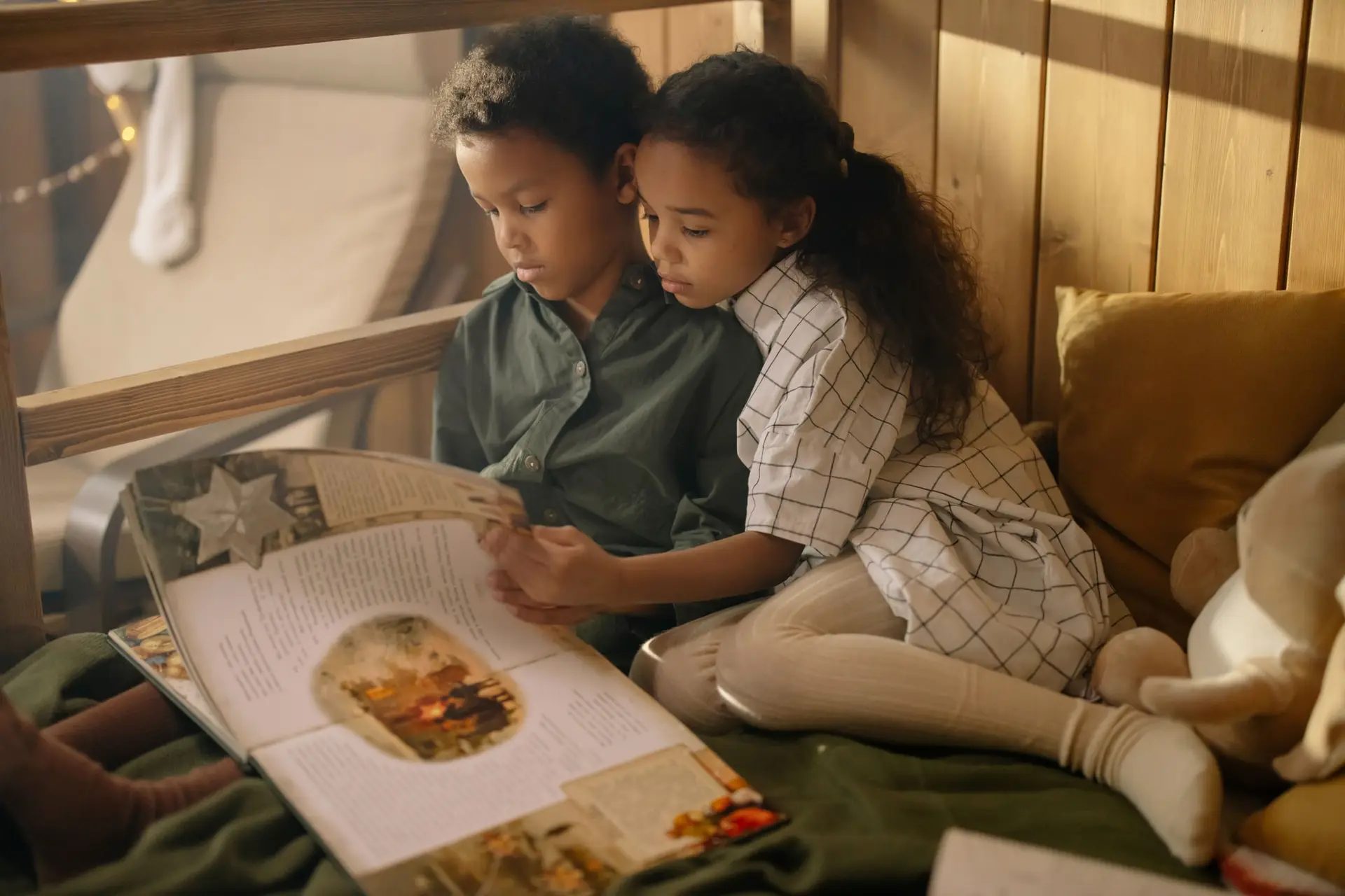 Dos niños leen juntos un libro ilustrado, sentados en un rincón de lectura.