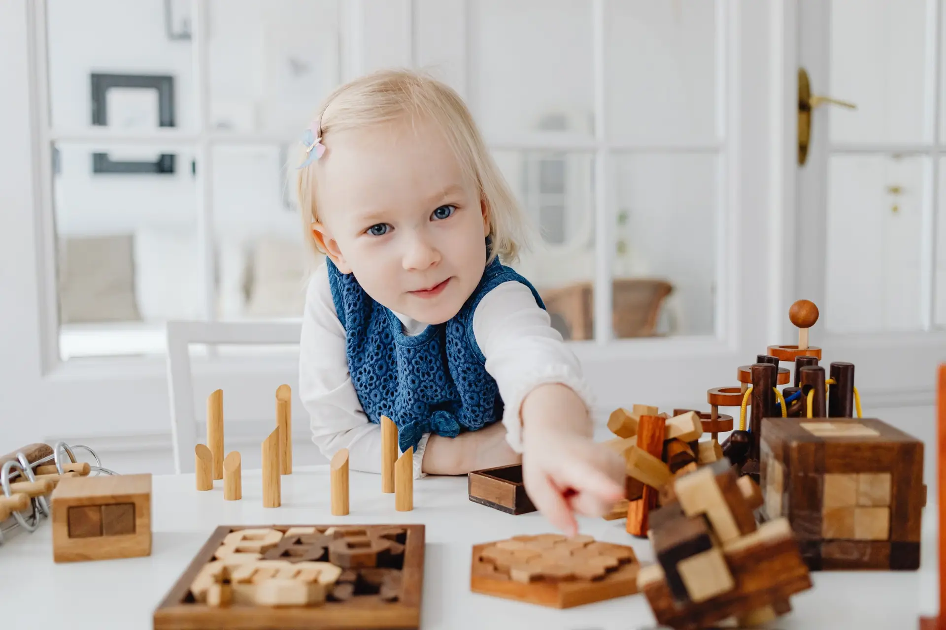 Un niño pequeño juega con un puzle y piezas de madera sobre una mesa blanca.